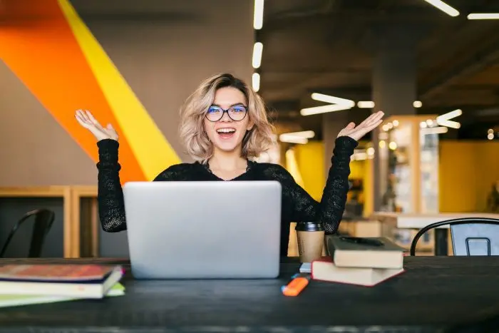 funny happy excited young pretty woman sitting table black shirt working laptop co working office wearing glasses scaled jpg